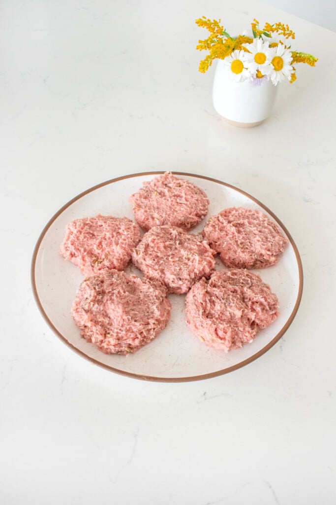 maple turkey breakfast sausages formed into patties on a plate on a marble counter with a vase of fresh flowers.