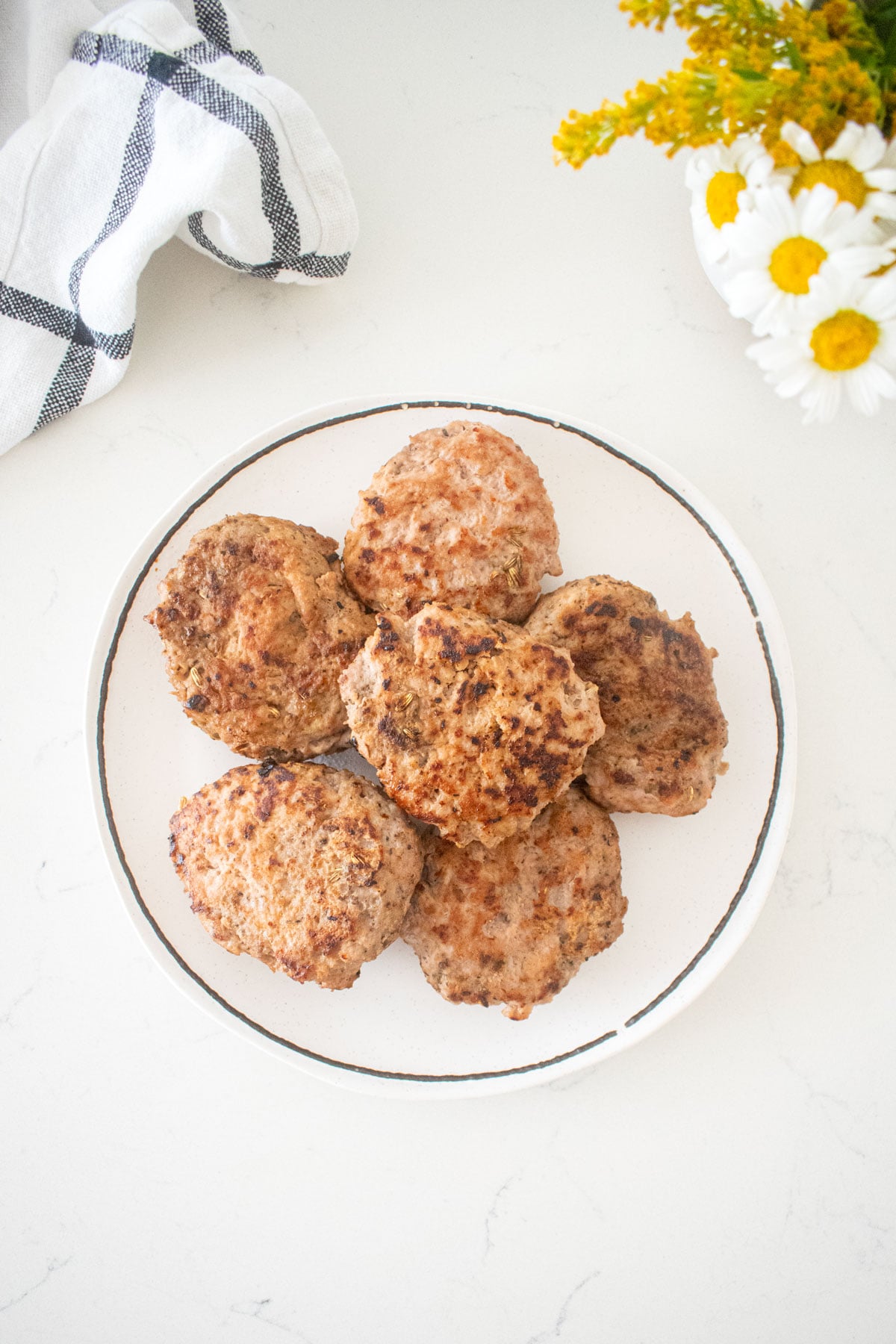 plate of maple turkey breakfast sausages on a marble counter with a vase of fresh flowers.