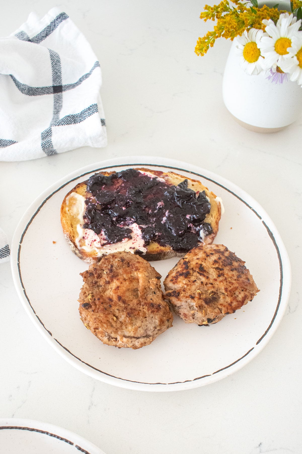 plate with two maple turkey breakfast sausage patties and a piece of sourdough toast with blueberry jam on a marble counter.