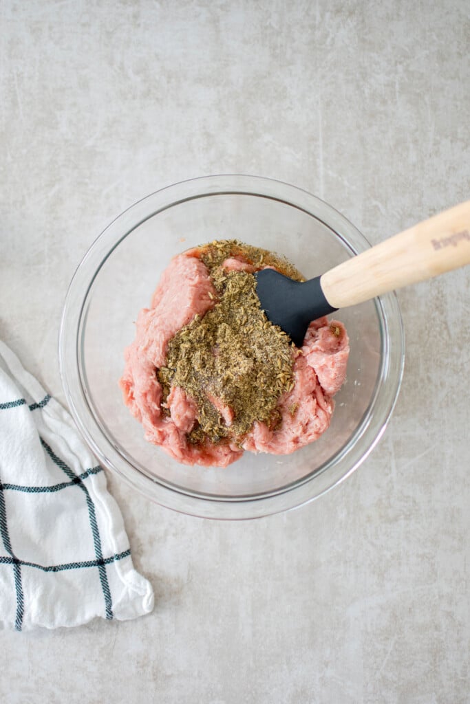 ground turkey and spices in a glass mixing bowl with a spatula.