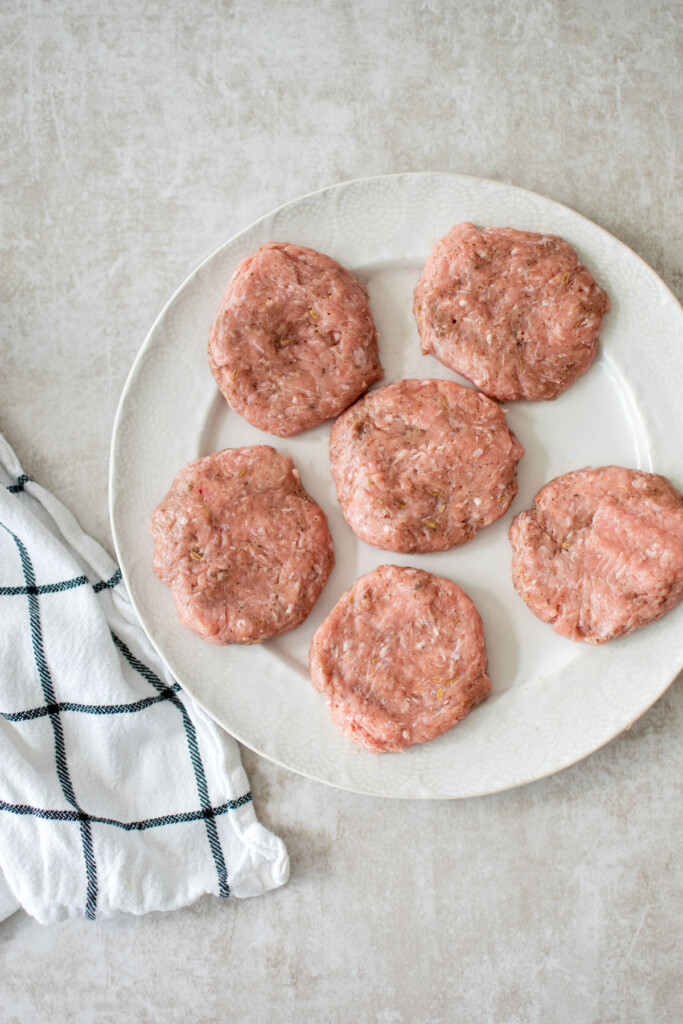 raw maple turkey breakfast sausage patties on a white plate.
