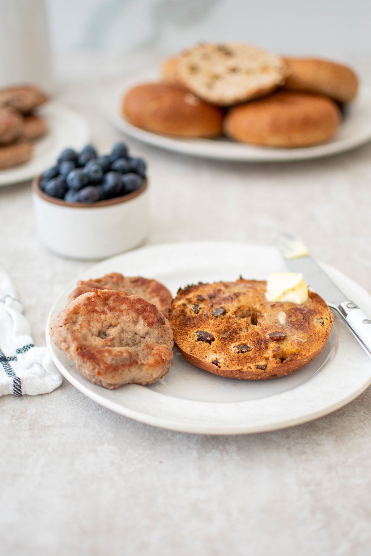 two maple turkey breakfast sausages on a plate with half a bagel with butter.