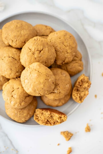 pumpkin peanut butter dog cookies on a plate on a white marble countertop.