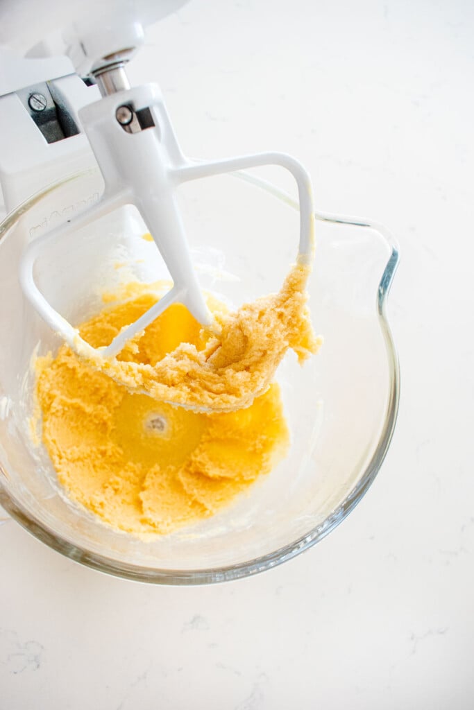 creamed butter, cane sugar and vanilla extract in a glass stand mixing bowl on a white marble counter.