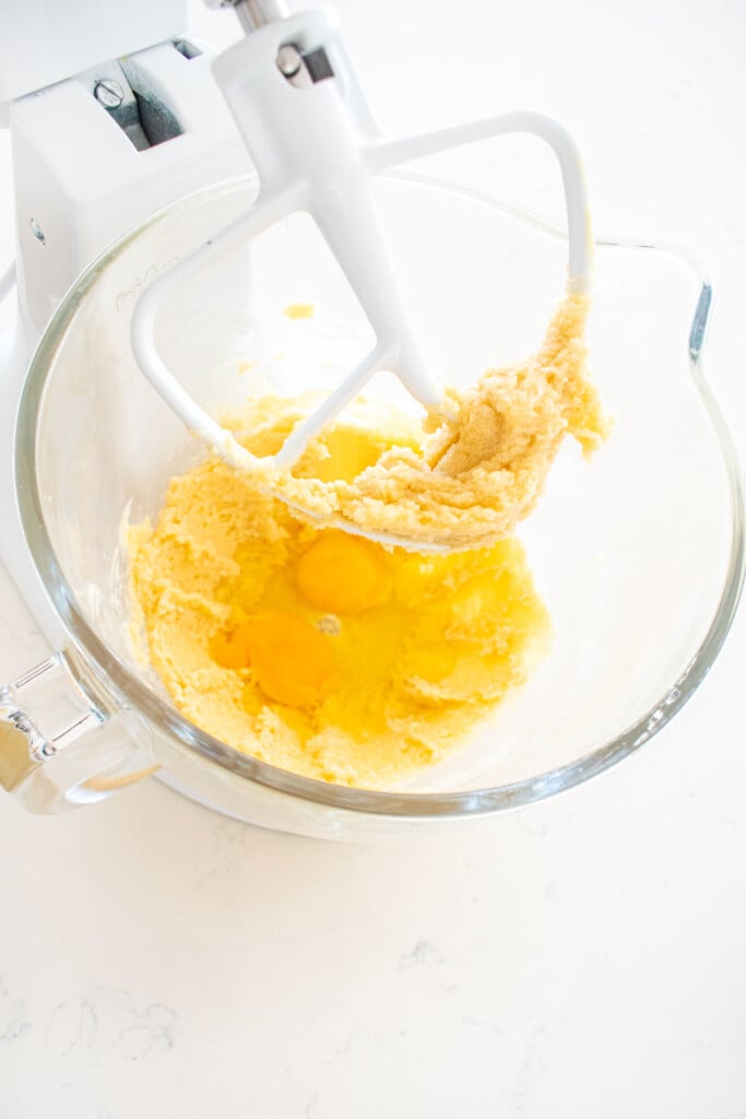 creamed butter, cane sugar, vanilla extract and 2 eggs in a glass stand mixing bowl on a white marble counter.