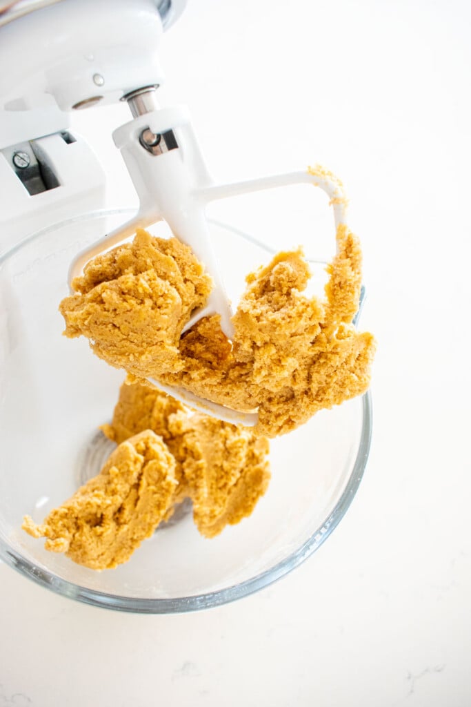 snickerdoodle cookie dough in a glass stand mixing bowl on a marble counter.