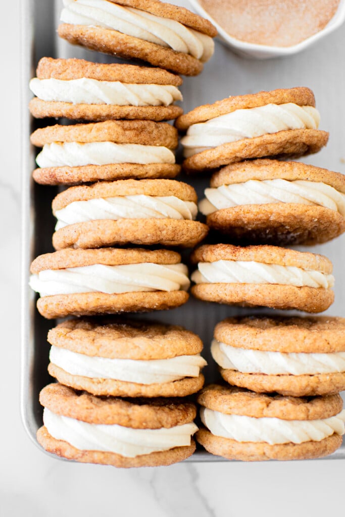 snickerdoodle sandwich cookies on a baking sheet on a white marble counter.