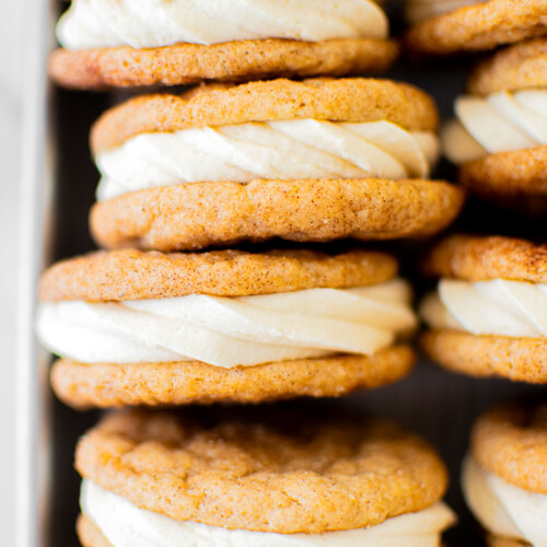 snickerdoodle sandwich cookies on a baking sheet on a white marble counter.
