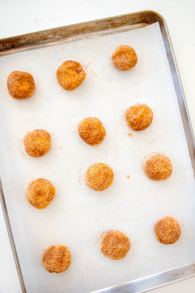 snickerdoodle cookie dough balls on a baking sheet on a white marble counter.