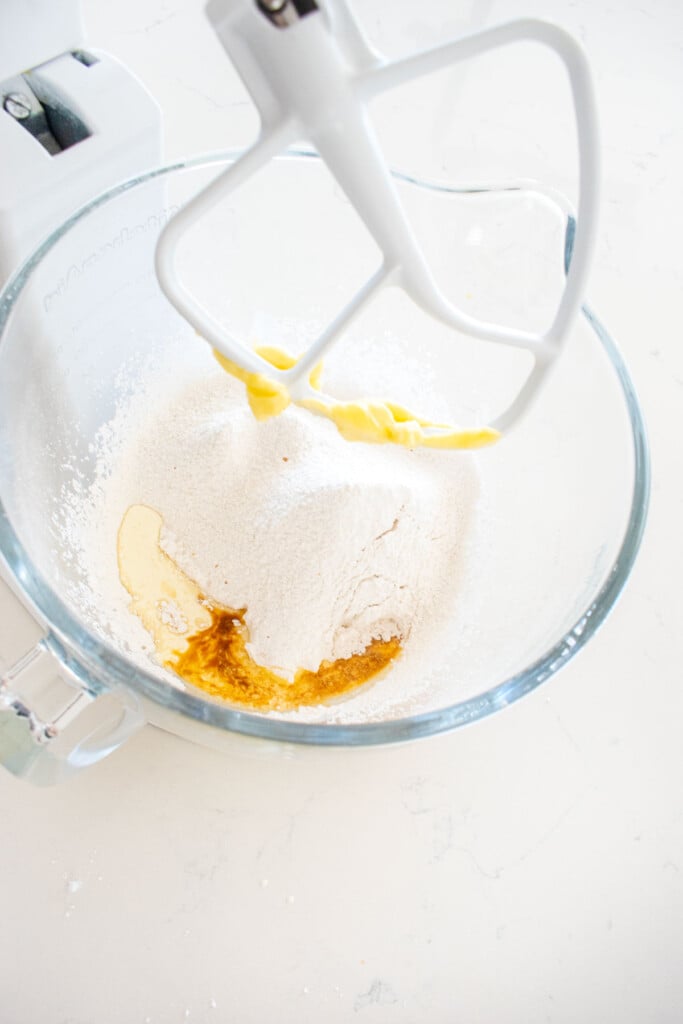 ingredients for vanilla buttercream frosting in a glass stand mixing bowl on a marble counter.
