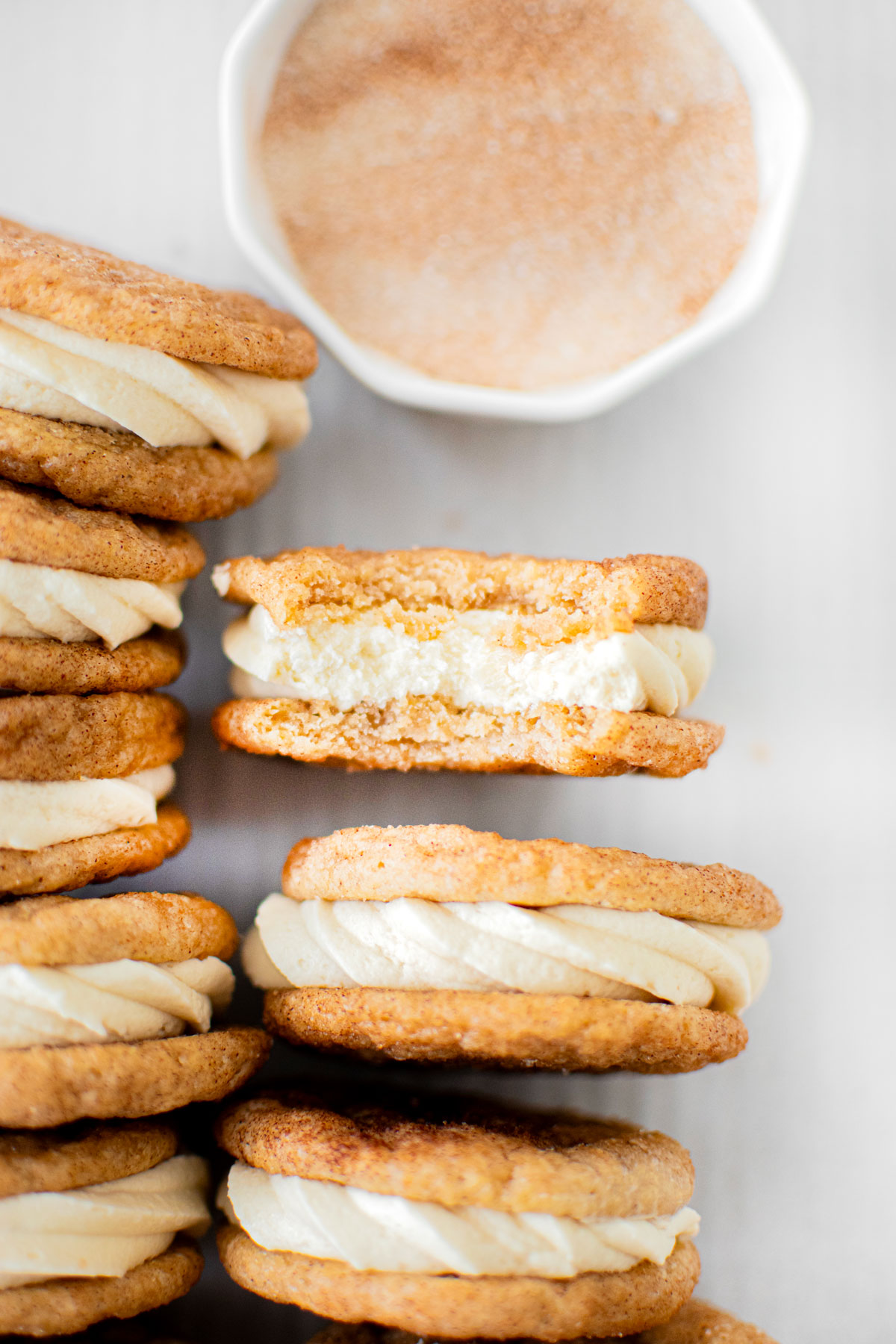 snickerdoodle sandwich cookies on a baking sheet one with a bite taken out on a white marble counter.
