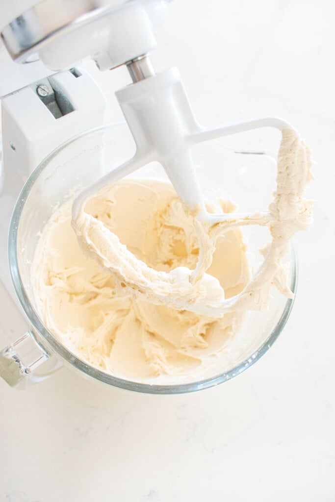 vanilla buttercream frosting in a glass stand mixing bowl on a marble counter.