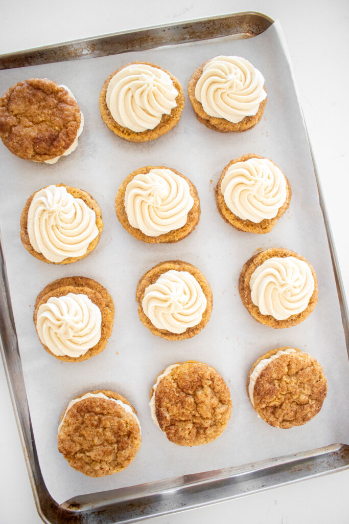 snickerdoodle cookies being filled with vanilla buttercream frosting swirls on a marble counter.