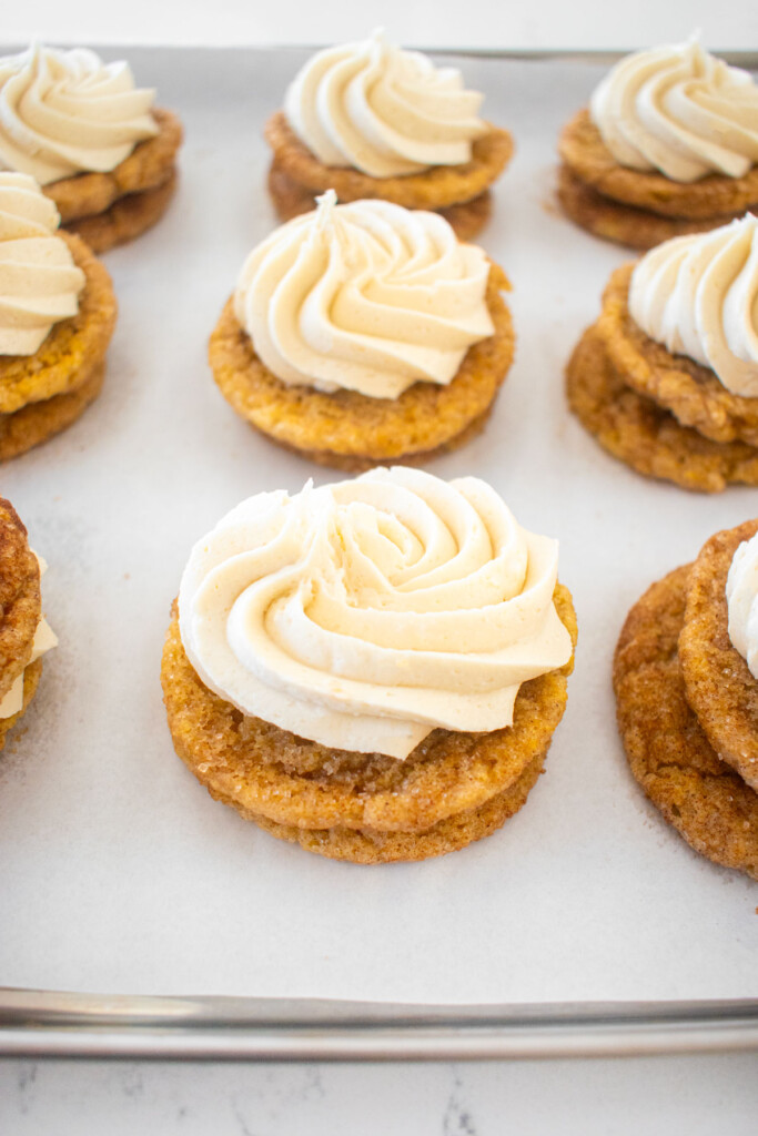 snickerdoodle cookies being filled with vanilla buttercream frosting swirls on a marble counter.