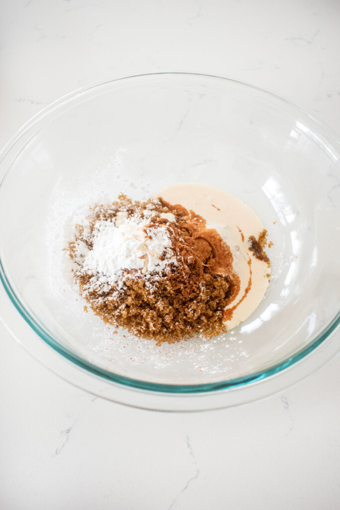 sourdough apple pie filing in a glass mixing bowl on a white marble counter.
