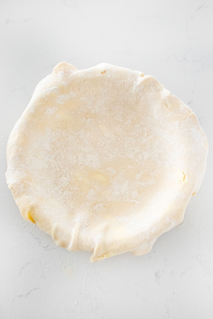sourdough pie crust in a pie pan on a white marble counter.