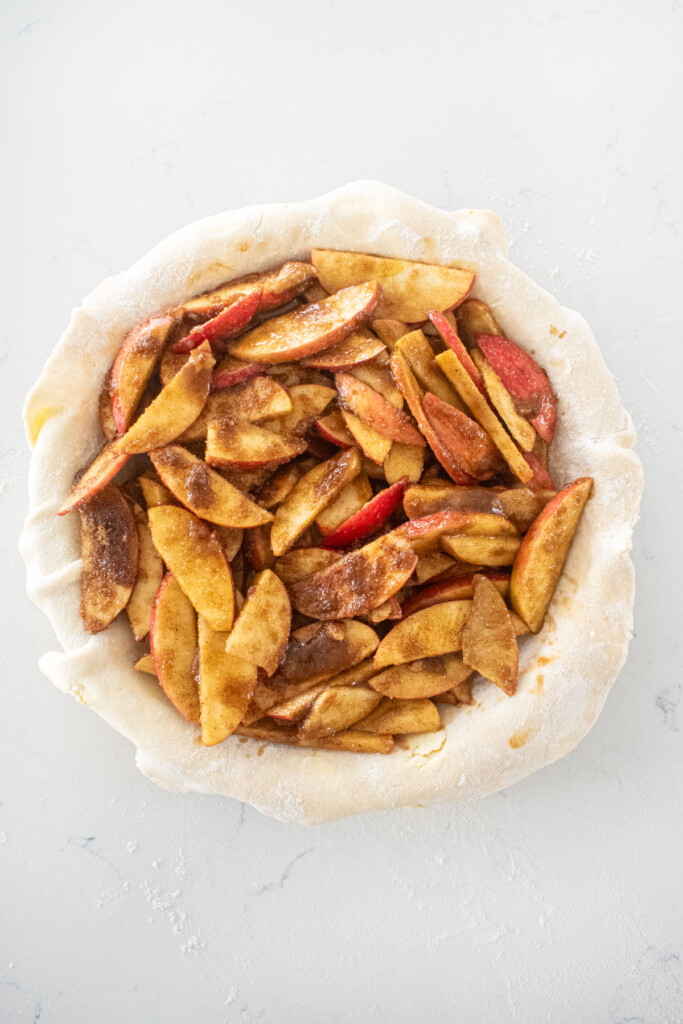 sourdough apple pie being assembled on a white marble counter.