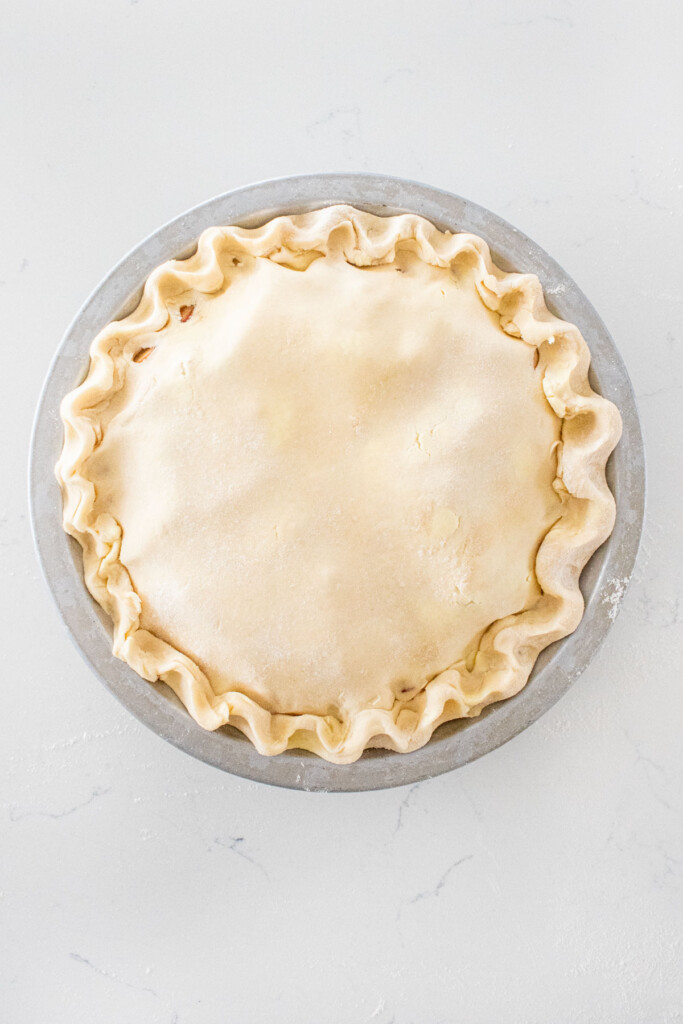 sourdough apple pie with fluted crust on a white marble counter.