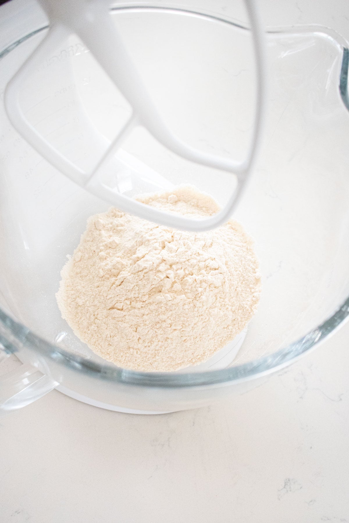 flour in a glass mixing bowl on a white marble counter.