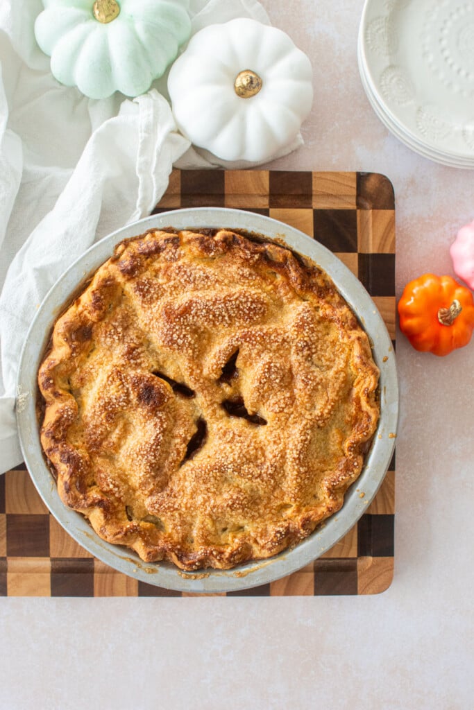 sourdough apple pie on a checkered cutting board with pumpkins and pie plates.