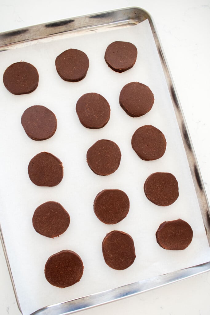 sourdough chocolate cookie dough disks on a baking sheet on a marble counter.