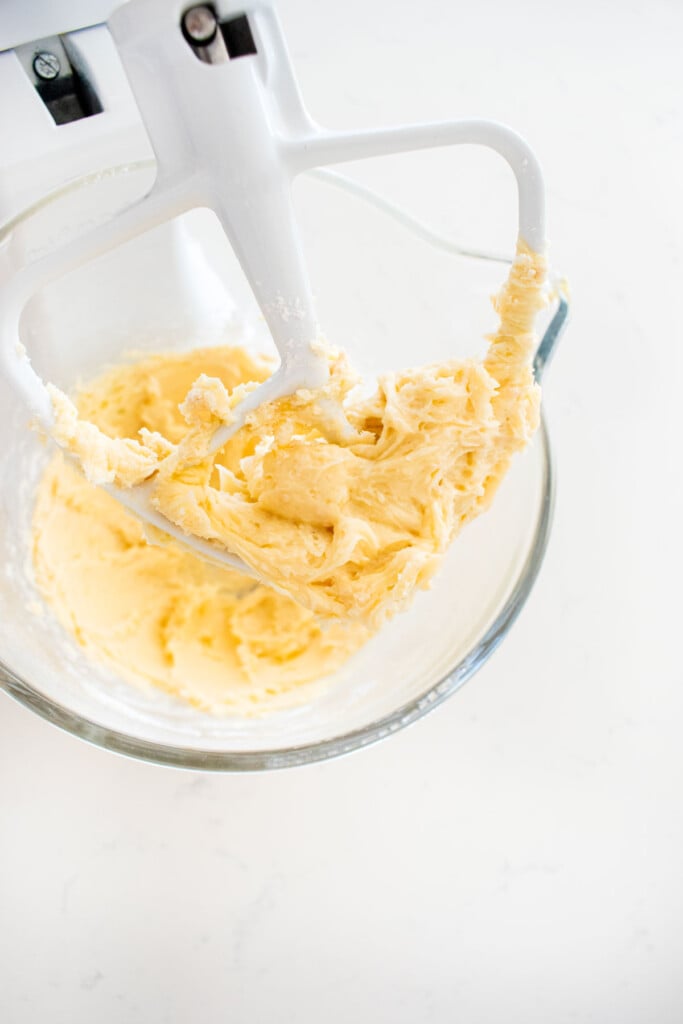 creamed butter and powdered sugar in a glass mixing bowl on a white marble counter.