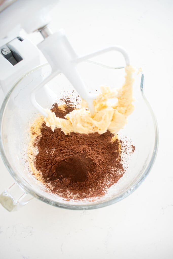 sourdough chocolate shortbread cookie dough ingredients in a glass stand mixing bowl on a white marble counter.