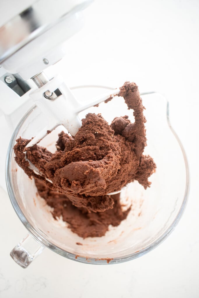 sourdough chocolate shortbread cookie dough in a glass stand mixing bowl on a white marble counter.