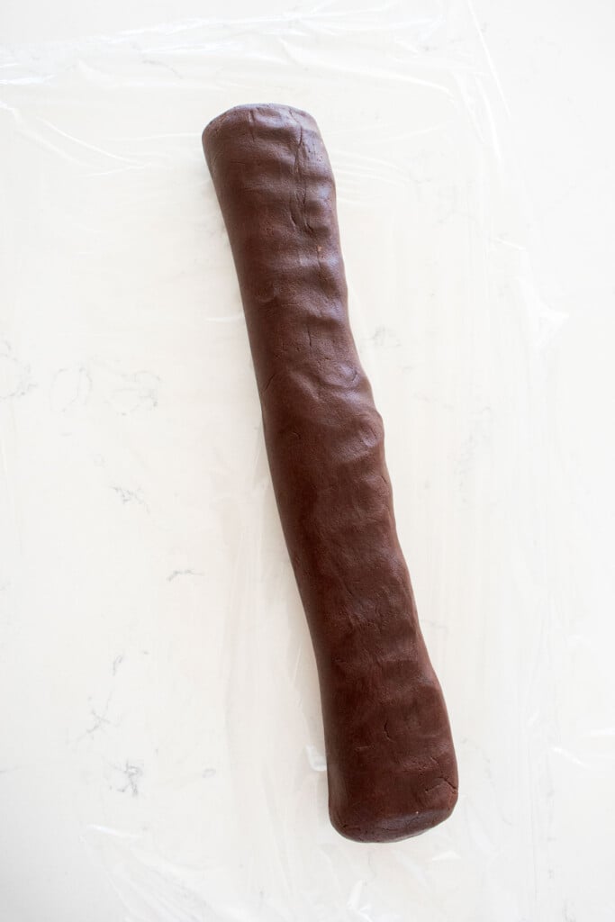 sourdough chocolate shortbread cookie dough rolled into a log on a piece of plastic wrap on a marble counter.