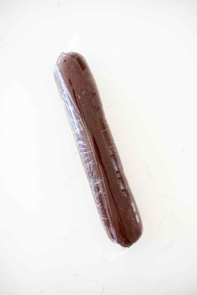sourdough chocolate shortbread cookie dough rolled into a log on a piece of plastic wrap on a marble counter.