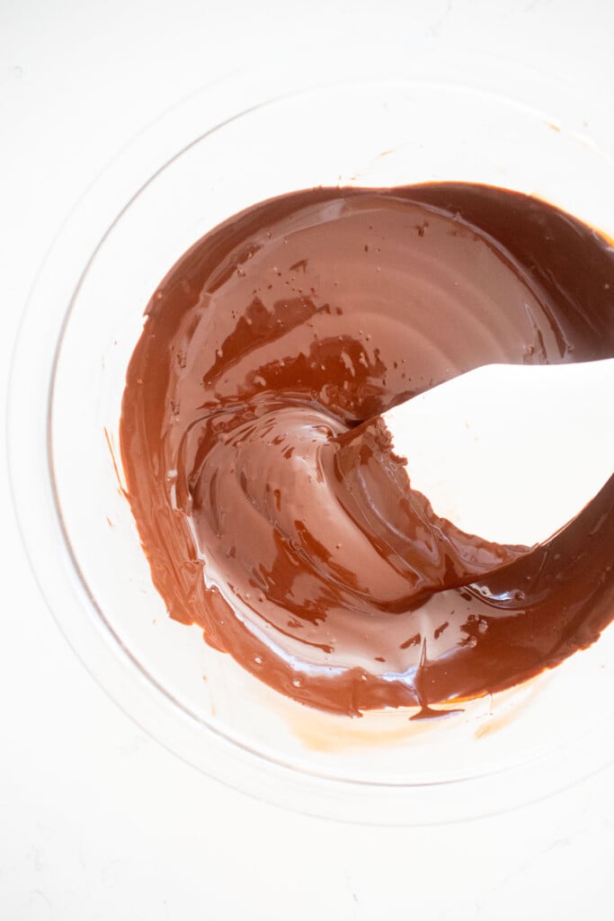 melted chocolate in a glass mixing bowl with a spatula on a marble counter.