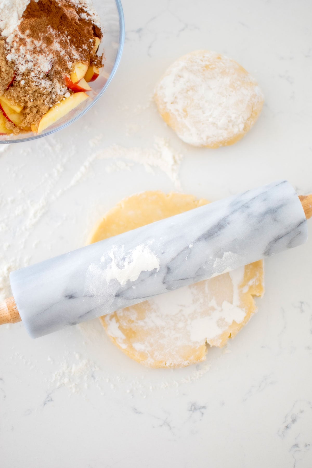 sourdough discard pie crust with flour and a marble rolling pin on a white marble counter.