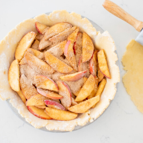 sourdough discard pie crust in a pie pan with apple pie filling on a marble counter with rolling pin.