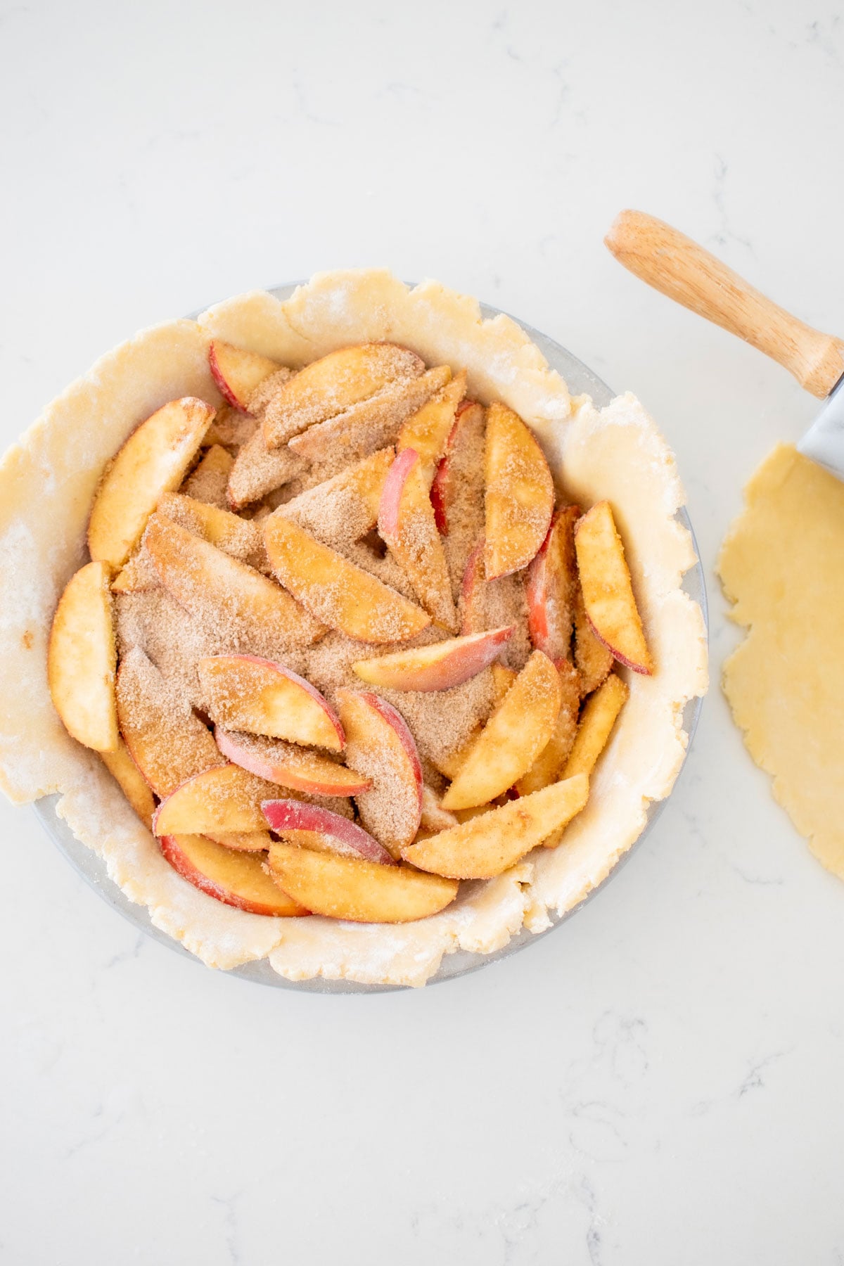 sourdough discard pie crust in a pie pan with apple pie filling on a marble counter with rolling pin.