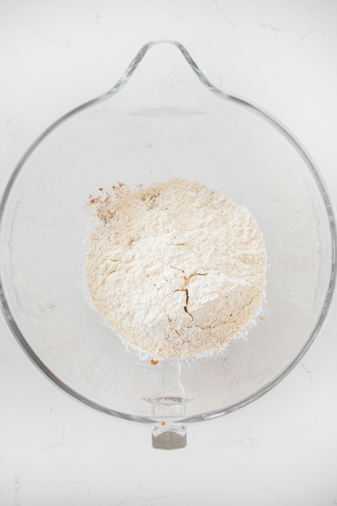 ingredients for vegan pumpkin spice cookie dough in a glass mixing bowl on a white countertop.
