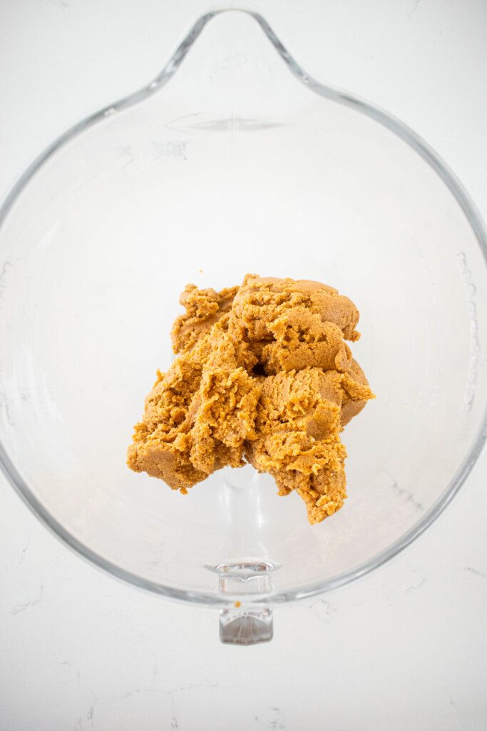 vegan pumpkin spice almond butter cookie dough in a glass mixing bowl on a white countertop.