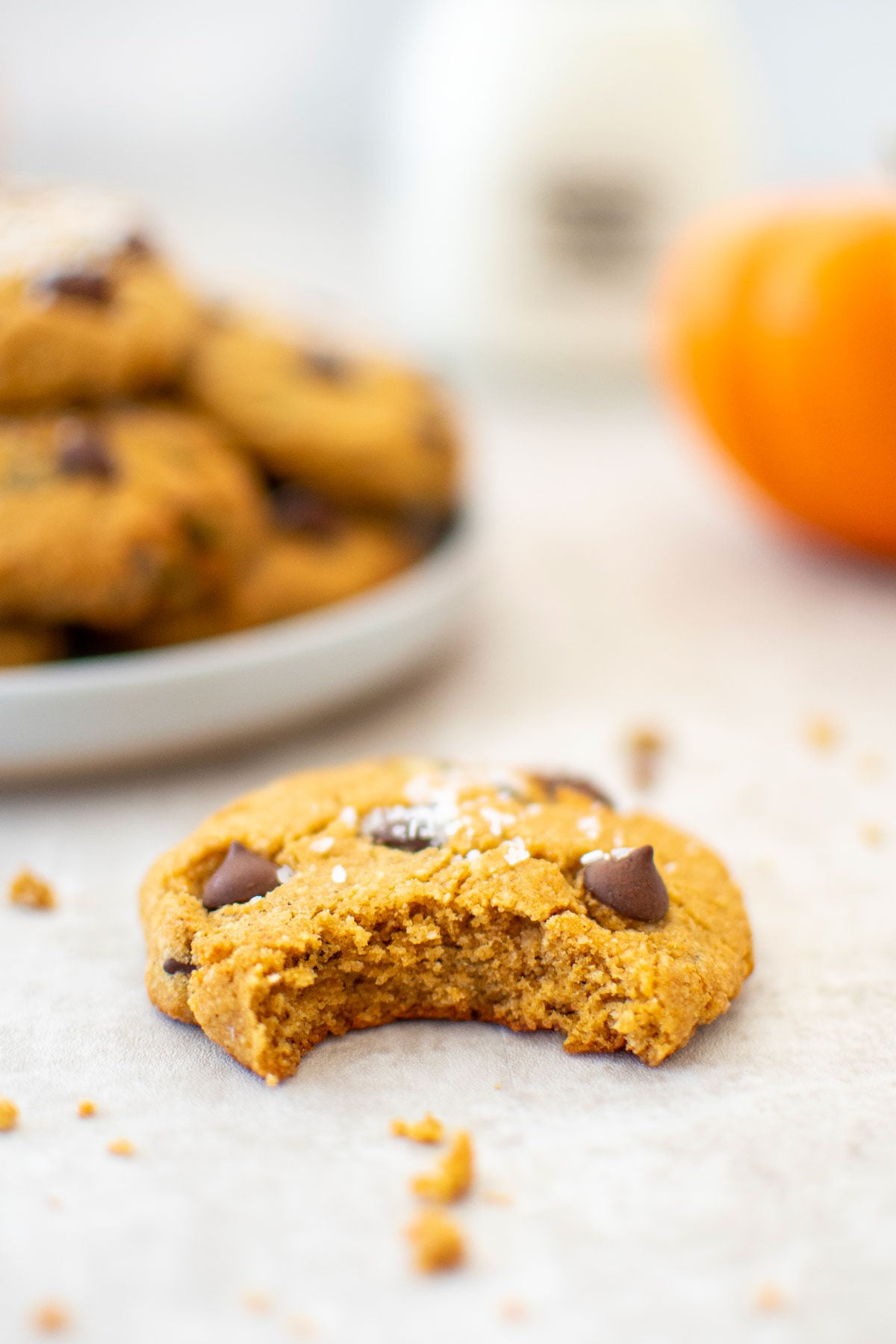 gluten free pumpkin chocolate chip cookie with a bite taken out on a tan table.