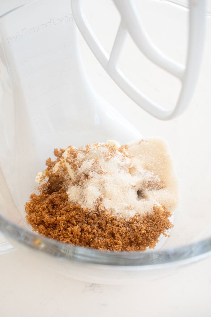 butter, dark brown sugar and cane sugar in a glass mixing bowl on a white marble counter.