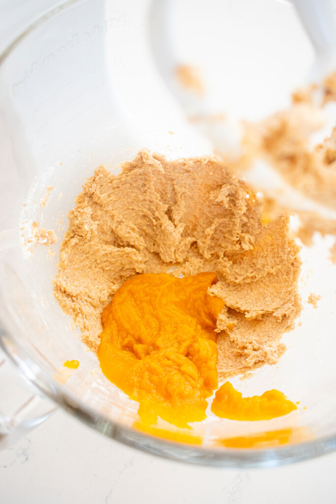 creamed butter and sugar with pumpkin puree in a glass mixing bowl on a white counter.