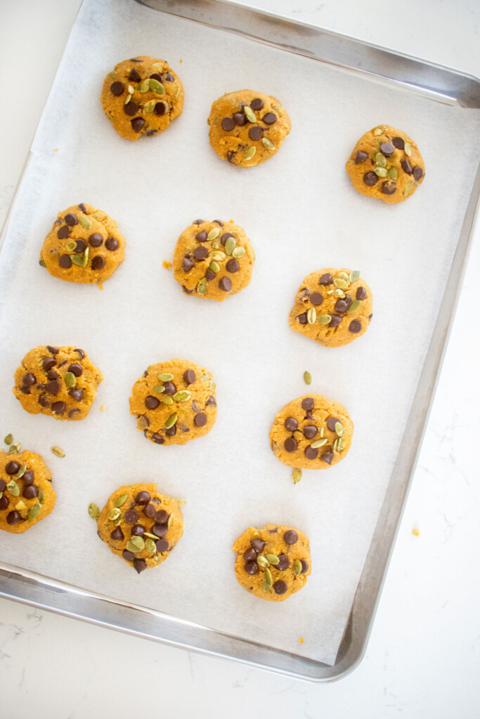 gluten free pumpkin chocolate chip cookie dough balls on a baking sheet on a white marble counter.