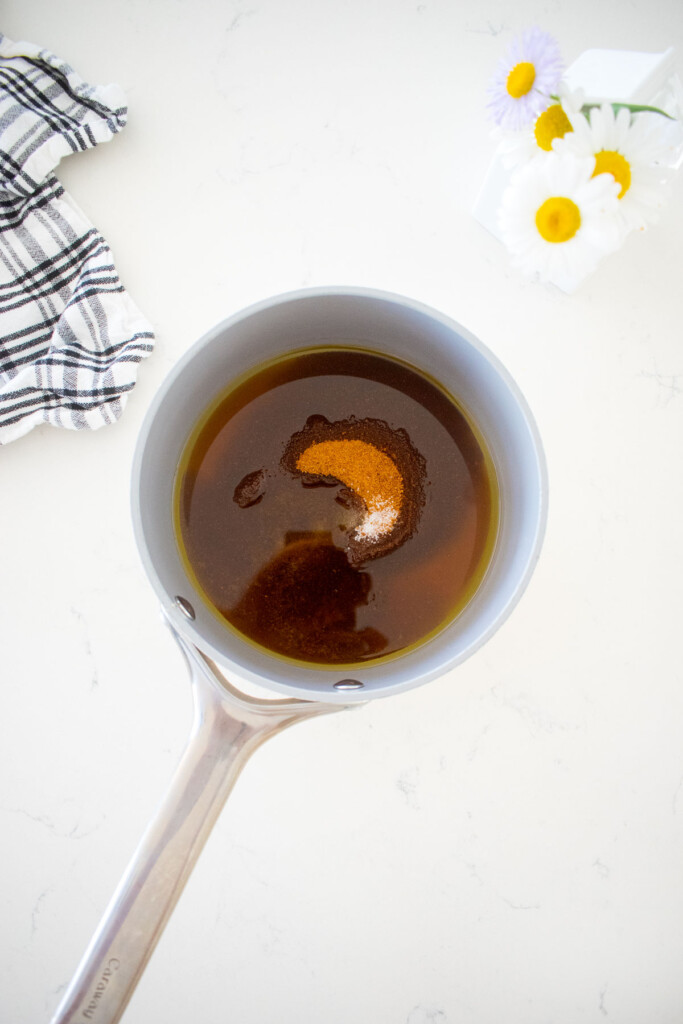 small pot with wet ingredients for chocolate olive oil granola on a marble counter with a vase of flowers.
