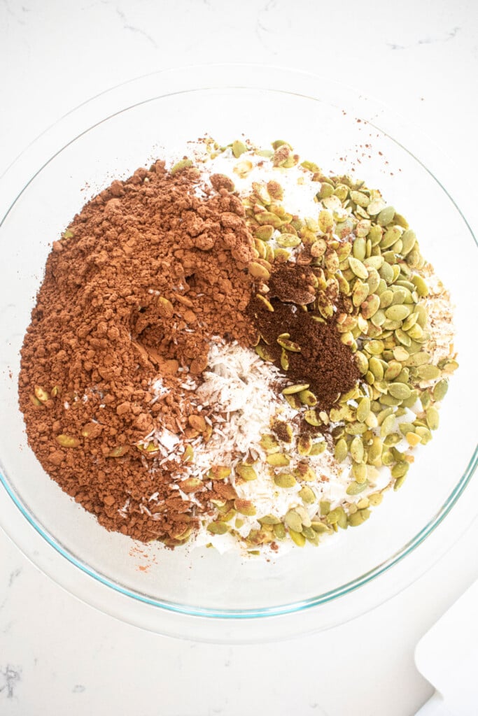 dry ingredients for chocolate olive oil granola in a glass mixing bowl on a white marble counter.