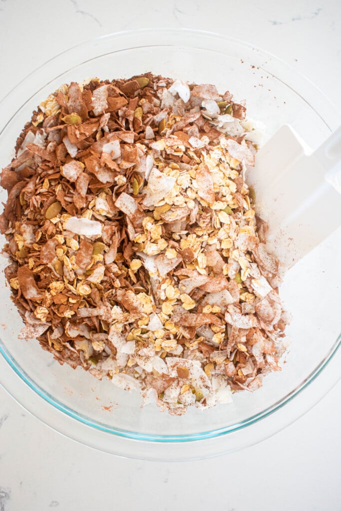dry ingredients for chocolate olive oil granola in a glass mixing bowl on a white marble counter.