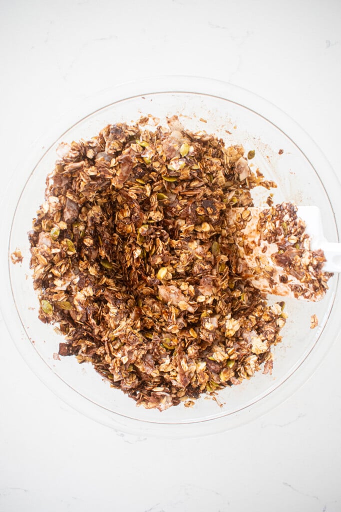 chocolate olive oil granola mixed together in a glass mixing bowl on a white marble counter.