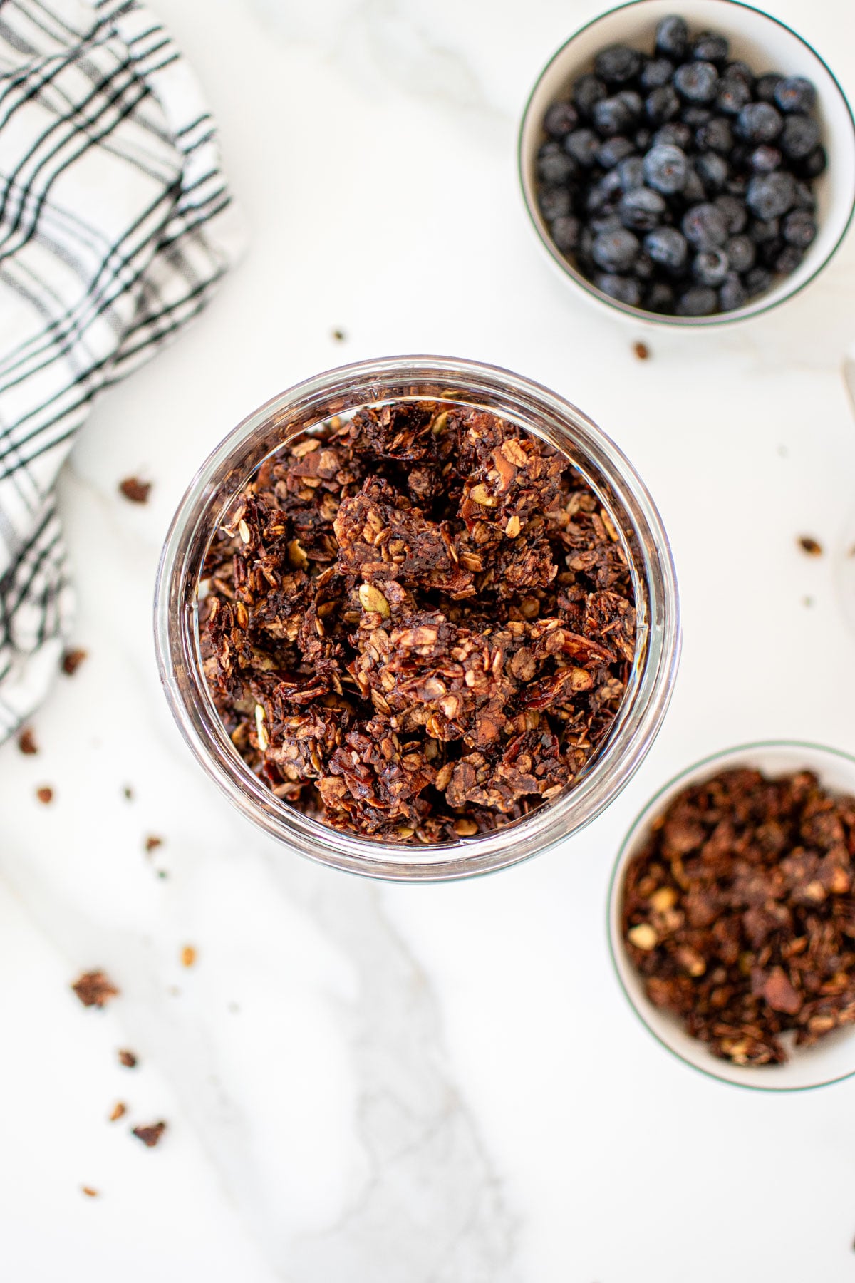 glass container of chocolate olive oil granola on a white marble counter.