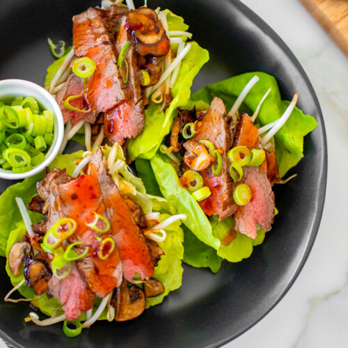 flank steak asian lettuce wraps in a black bowl on a white marble countertop.