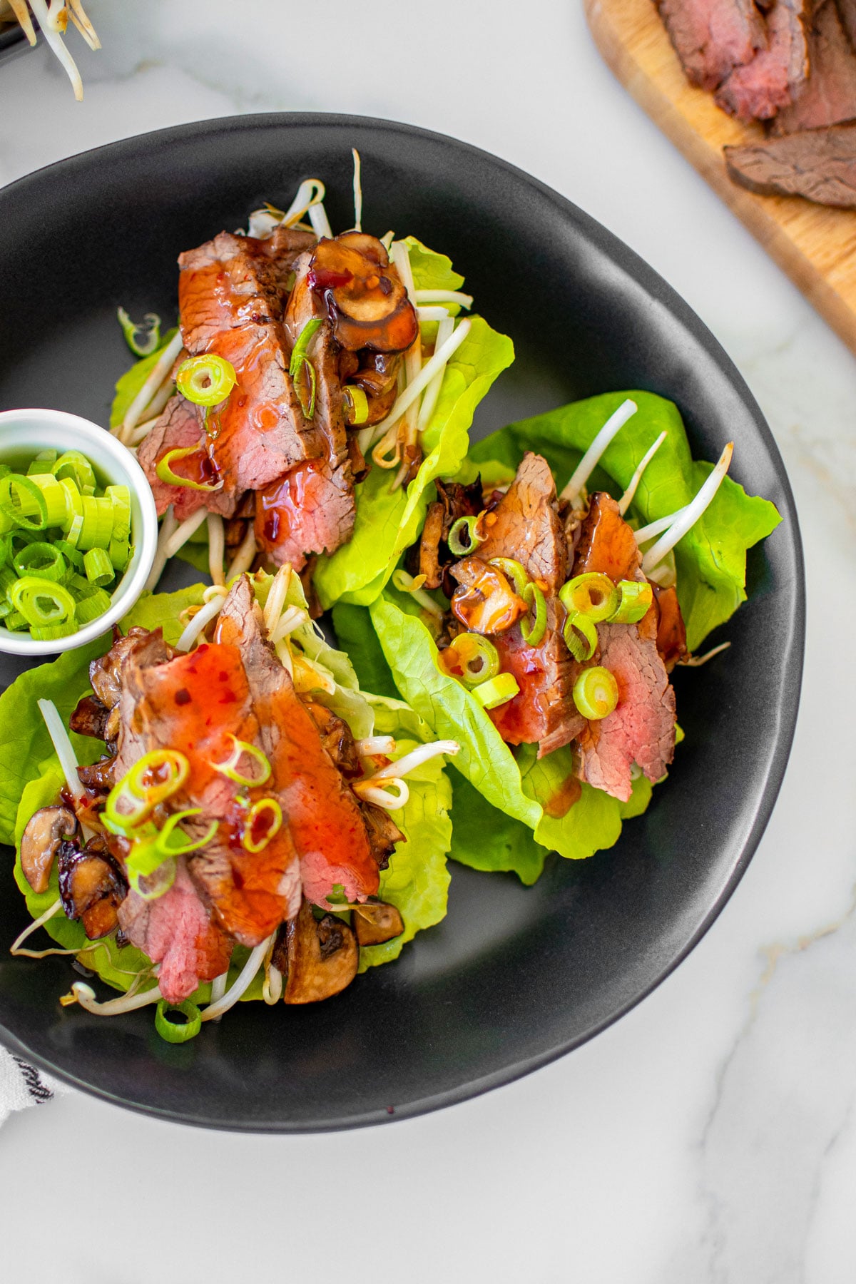 flank steak asian lettuce wraps in a black bowl on a white marble countertop.