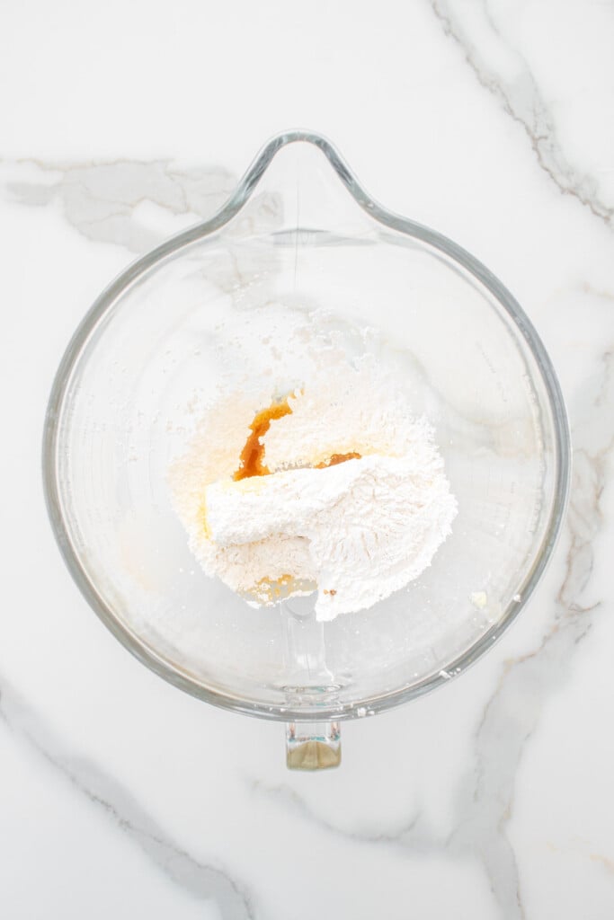 butter powdered sugar and vanilla in a glass mixing bowl on a white marble counter.