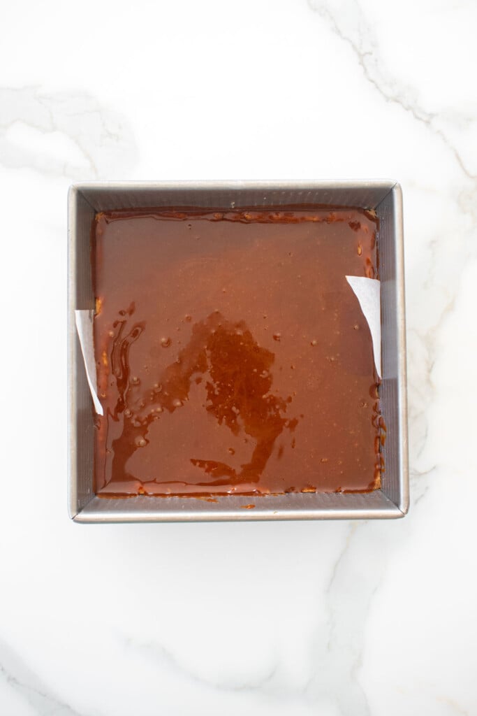 caramel on top of cookie layer in a baking pan on a marble counter.