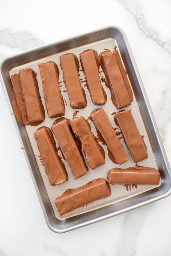 homemade twix bars on a baking sheet on a marble counter.